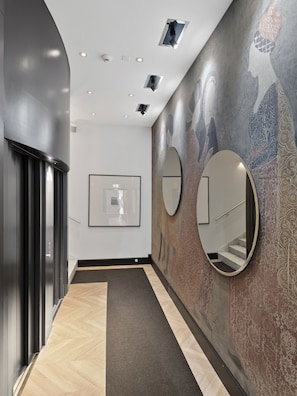 A modern hallway with a polished floor, a staircase, and a wall with decorative patterns and mirrors.