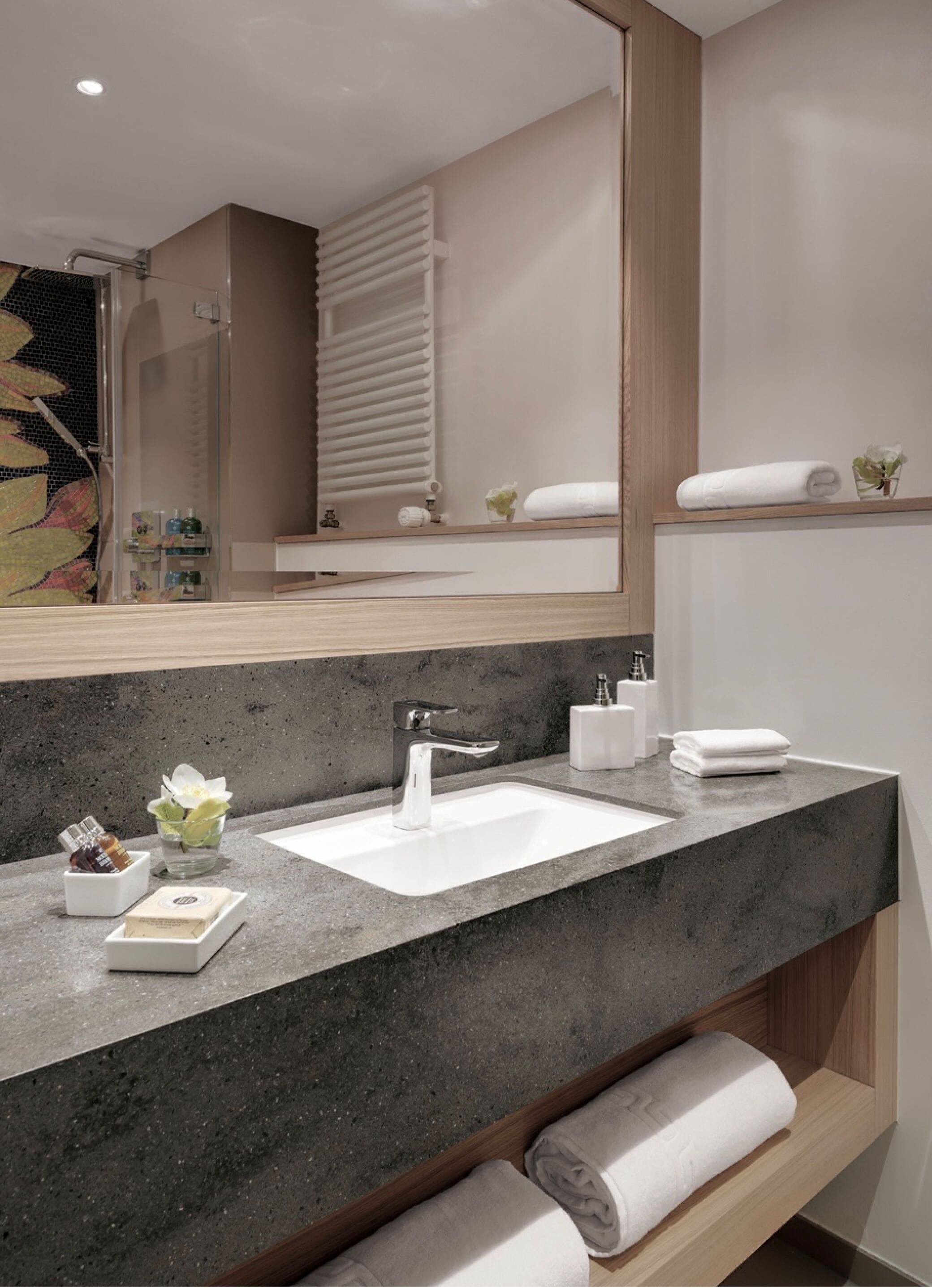 Ein modernes Badezimmer mit einer Granittafel, einem weißen Waschbecken und einem großen Spiegel.