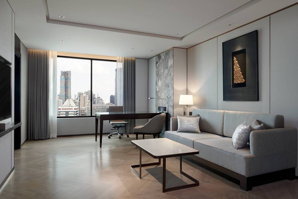A modern hotel room with a large window, a sofa, a table, and a TV.