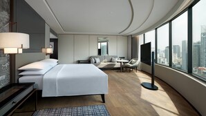 Una habitación de hotel moderna con una cama grande, un escritorio, una silla, un televisor y vistas a la ciudad.