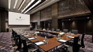 A JW Marriott conference room with long tables, chairs, and a large screen displaying the hotel name.