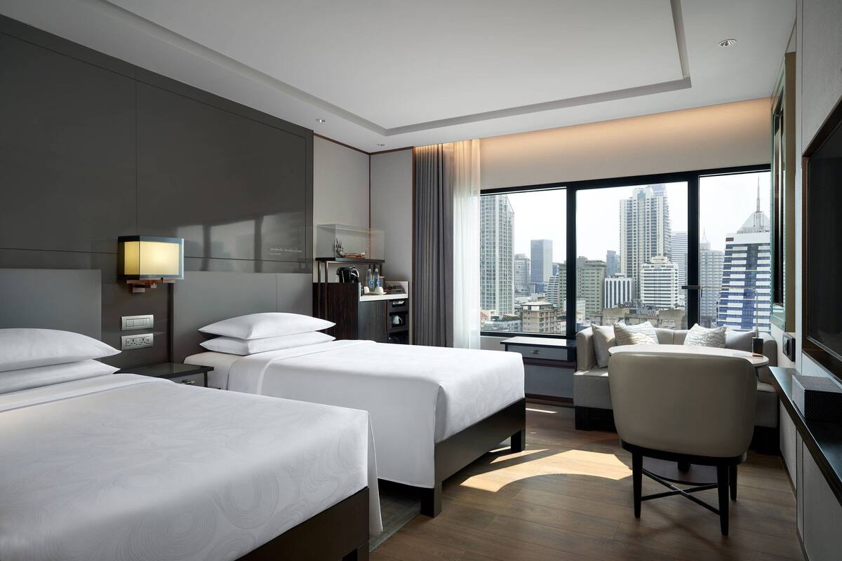 A hotel room with two beds, a sofa, a TV, and a city view.