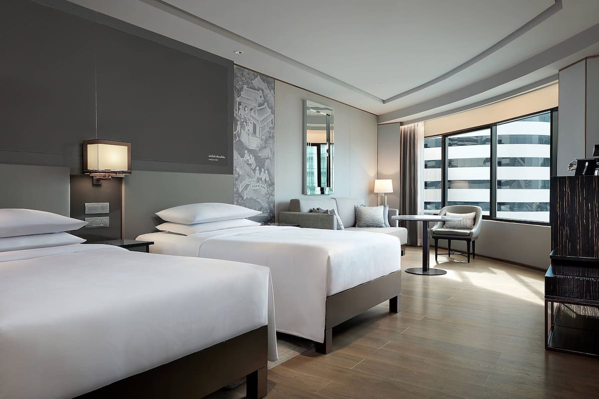 A hotel room with two beds, a desk, a chair, and a large window.