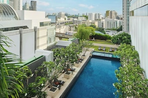 A rooftop pool with a cityscape view, surrounded by greenery and modern architecture.