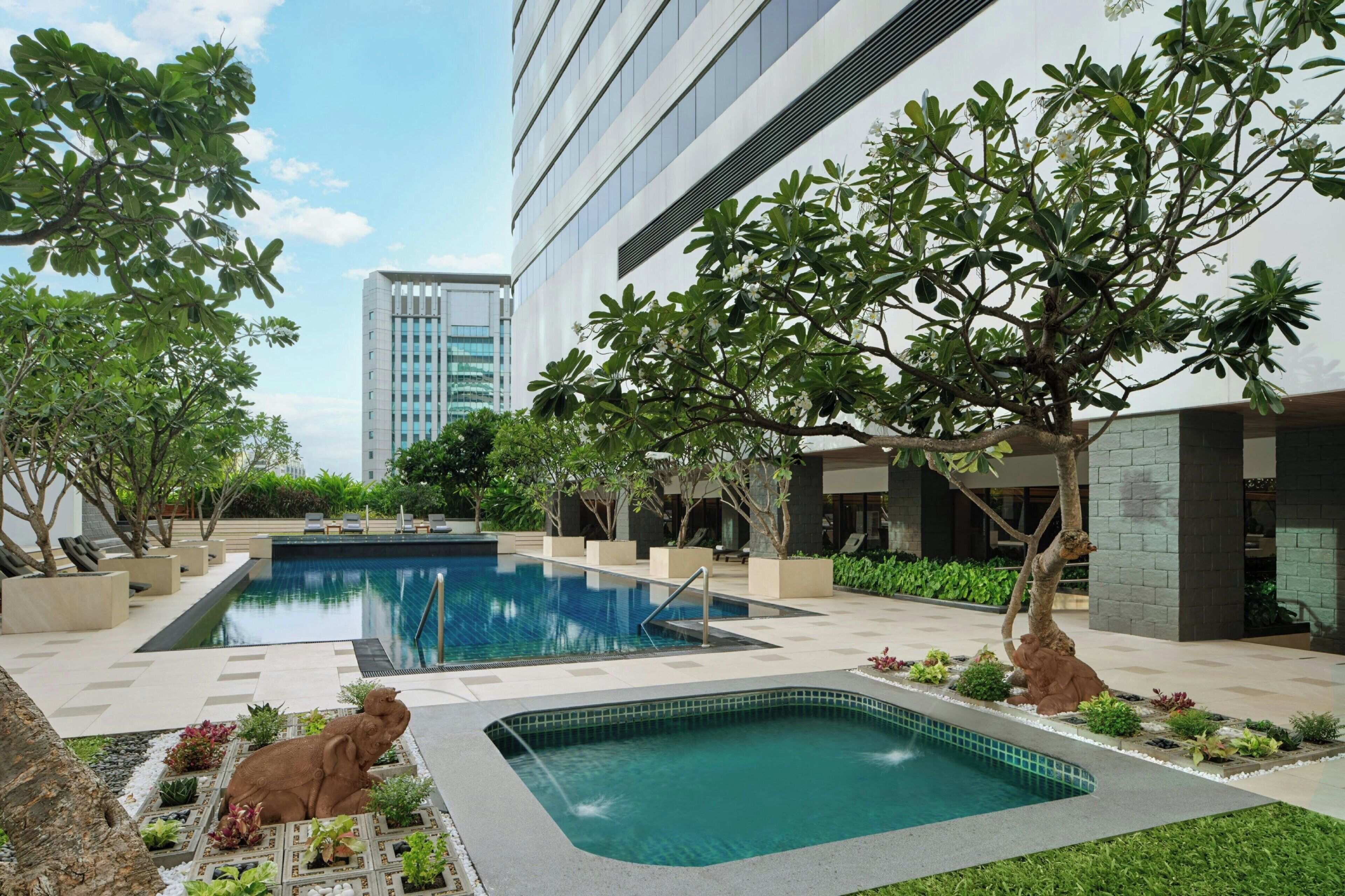 A pool area with two pools, surrounded by greenery and modern buildings.