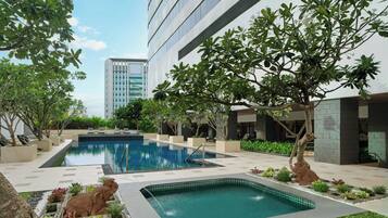 A pool area with two pools, surrounded by greenery and modern buildings.