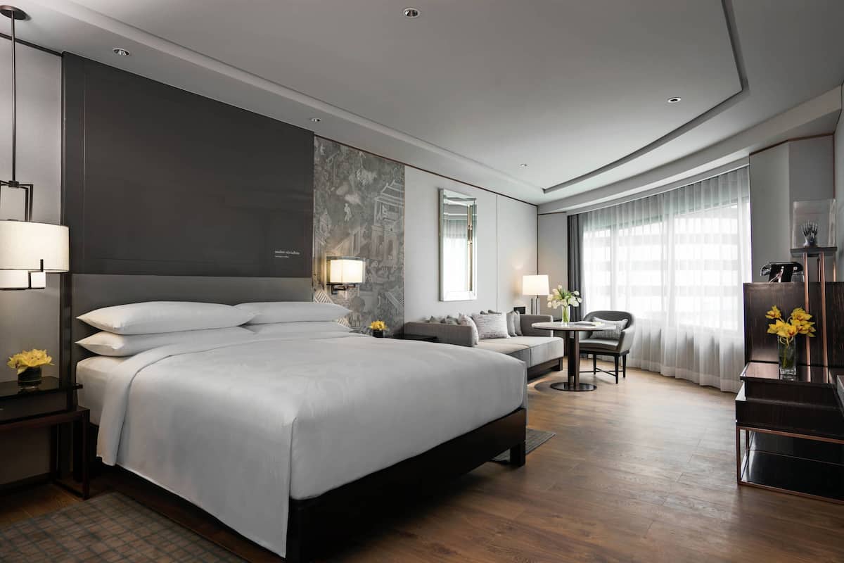 A modern hotel room with a large bed, a desk, a chair, and a small table.