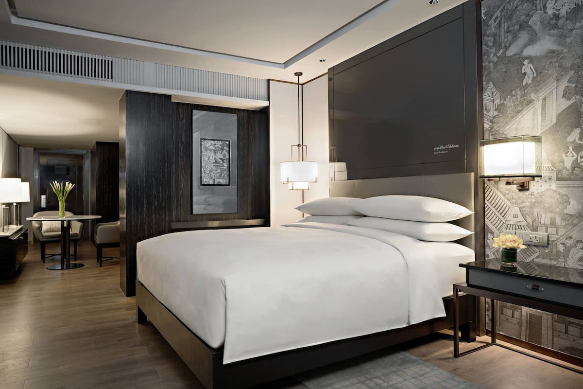 A modern hotel room with a large bed, a desk, a chair, and a wall-mounted TV.