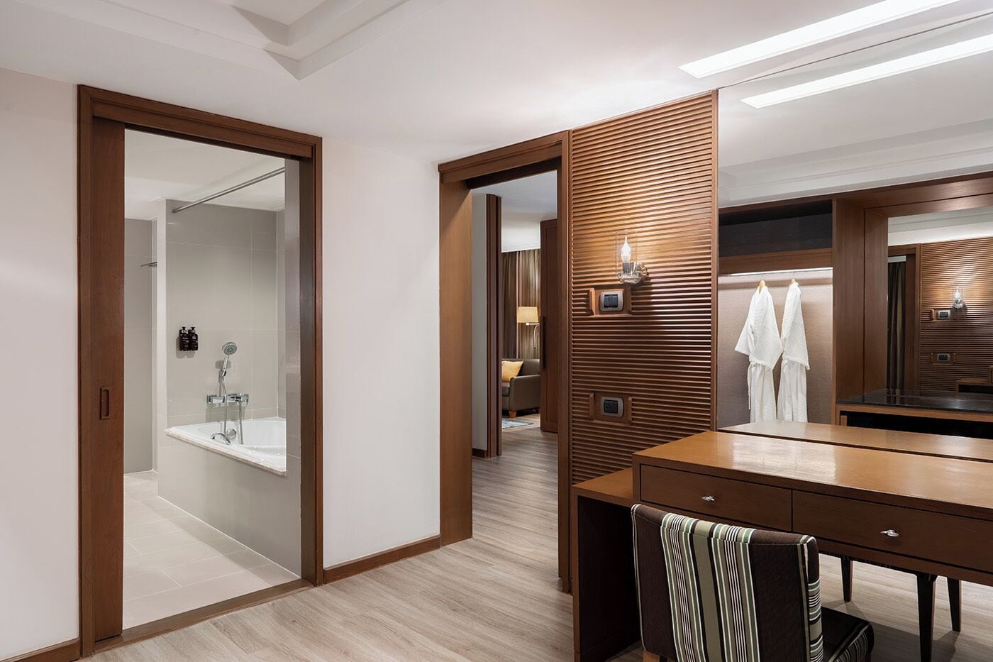 A modern hotel bathroom with a glass-enclosed shower, wooden paneling, and a vanity with a mirror.