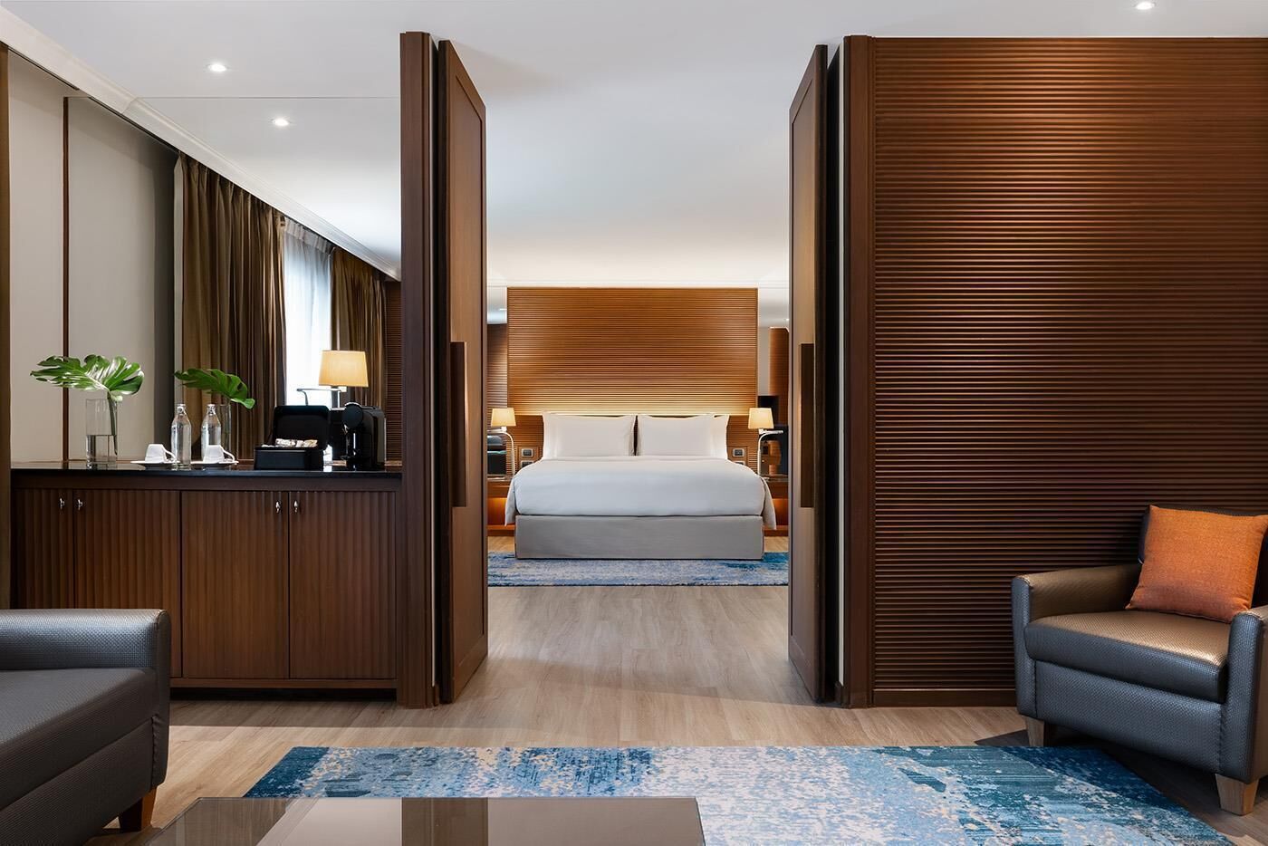 A hotel room with a bed, a desk, a chair, and a large wooden panel wall.