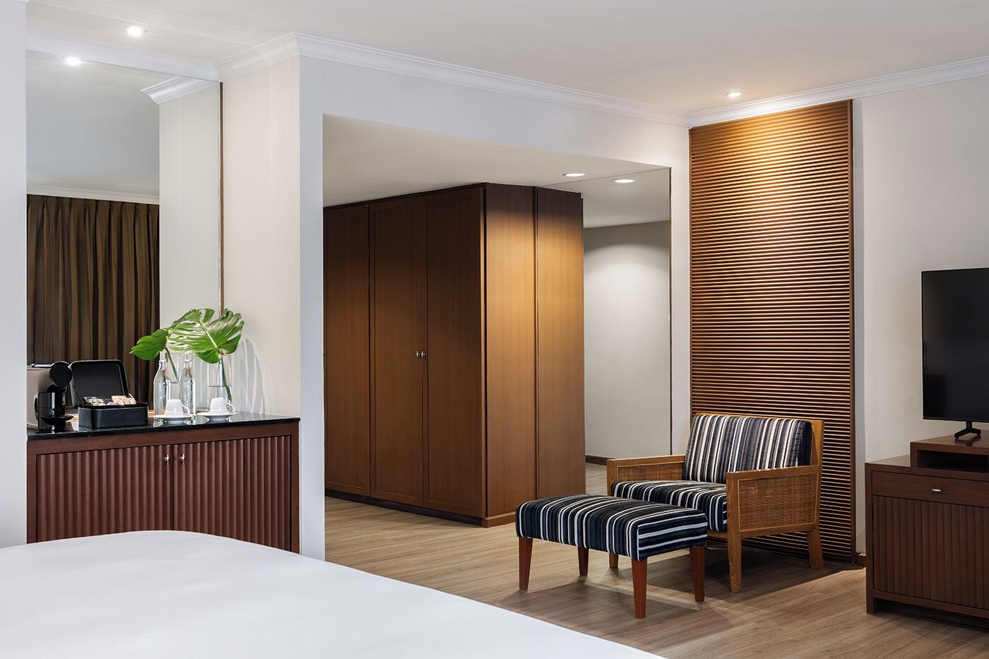 Een moderne hotelkamer met een groot bed, een houten garderobe, een gestreept fauteuil, een televisie en een koffieapparaat op het bureau.