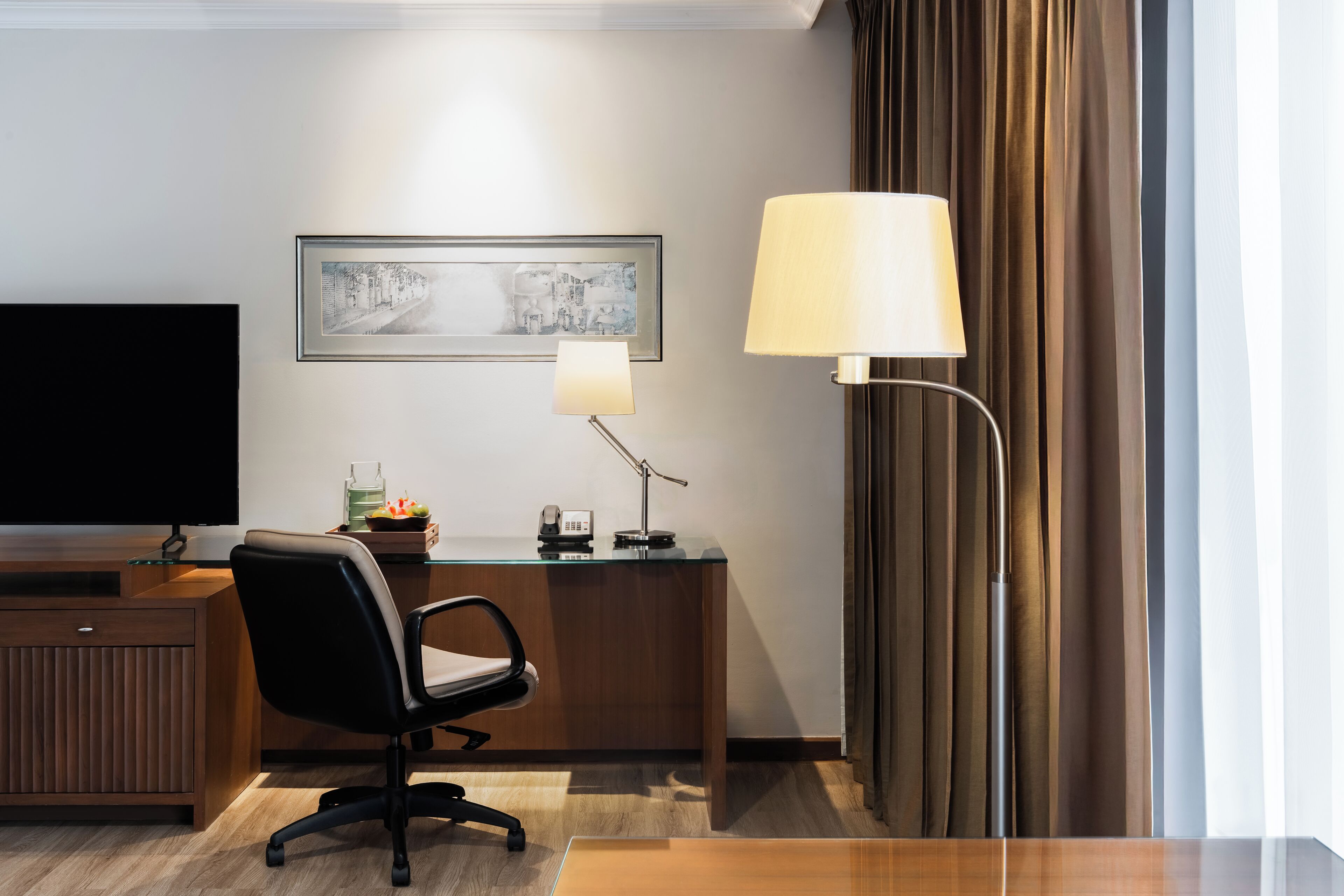 A hotel room with a desk, chair, television, lamp, and a framed picture on the wall.