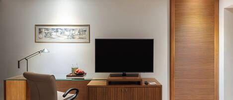 A modern hotel room with a wooden desk, a flat-screen TV, a framed picture, a lamp, and a wooden partition.