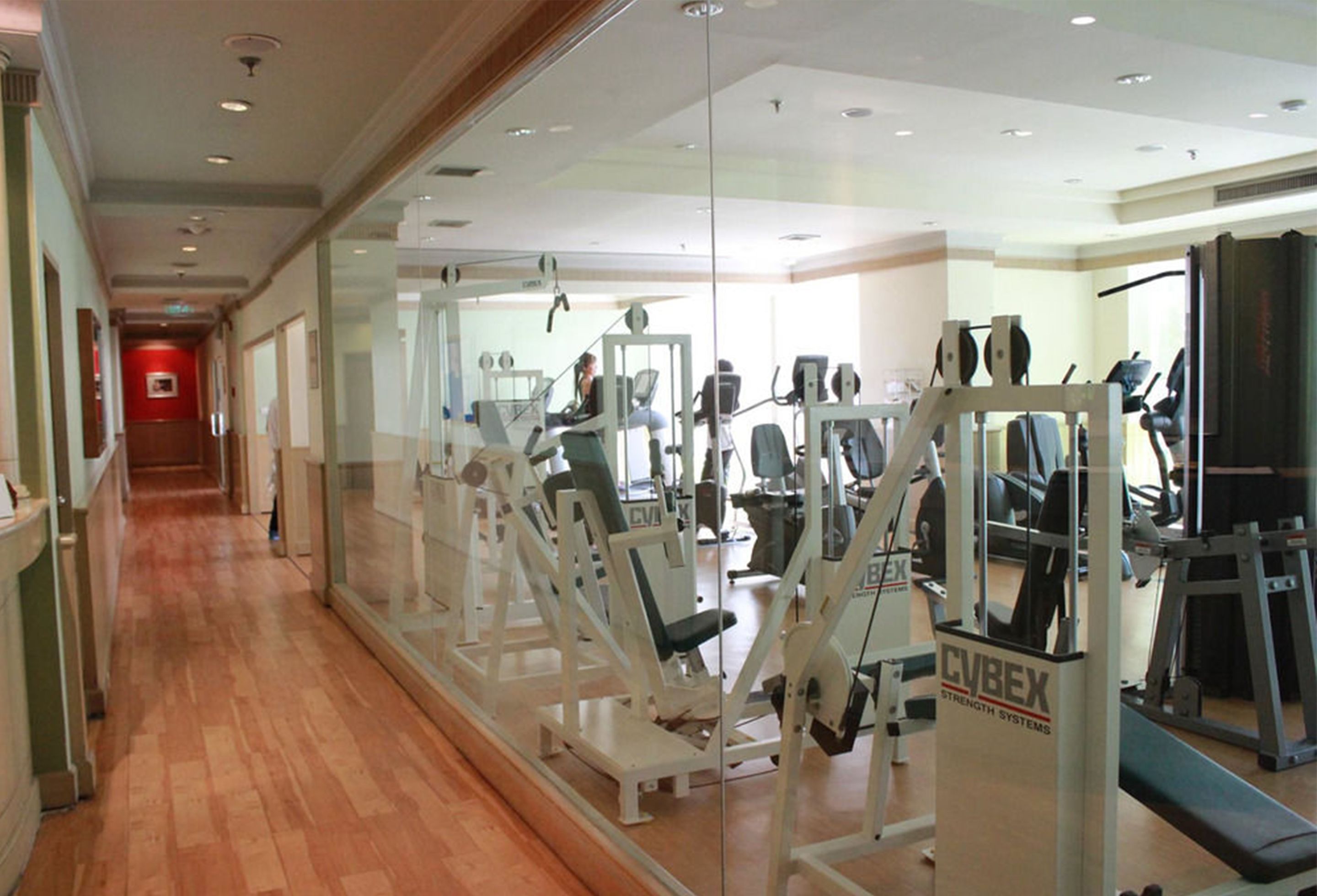 A gym with various exercise machines, a wooden floor, and a glass wall.