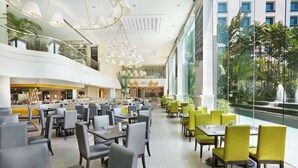 A spacious hotel lobby with multiple dining areas, a central staircase, and a view of a fountain. - Dusit Princess Srinakarin (Bangkok)