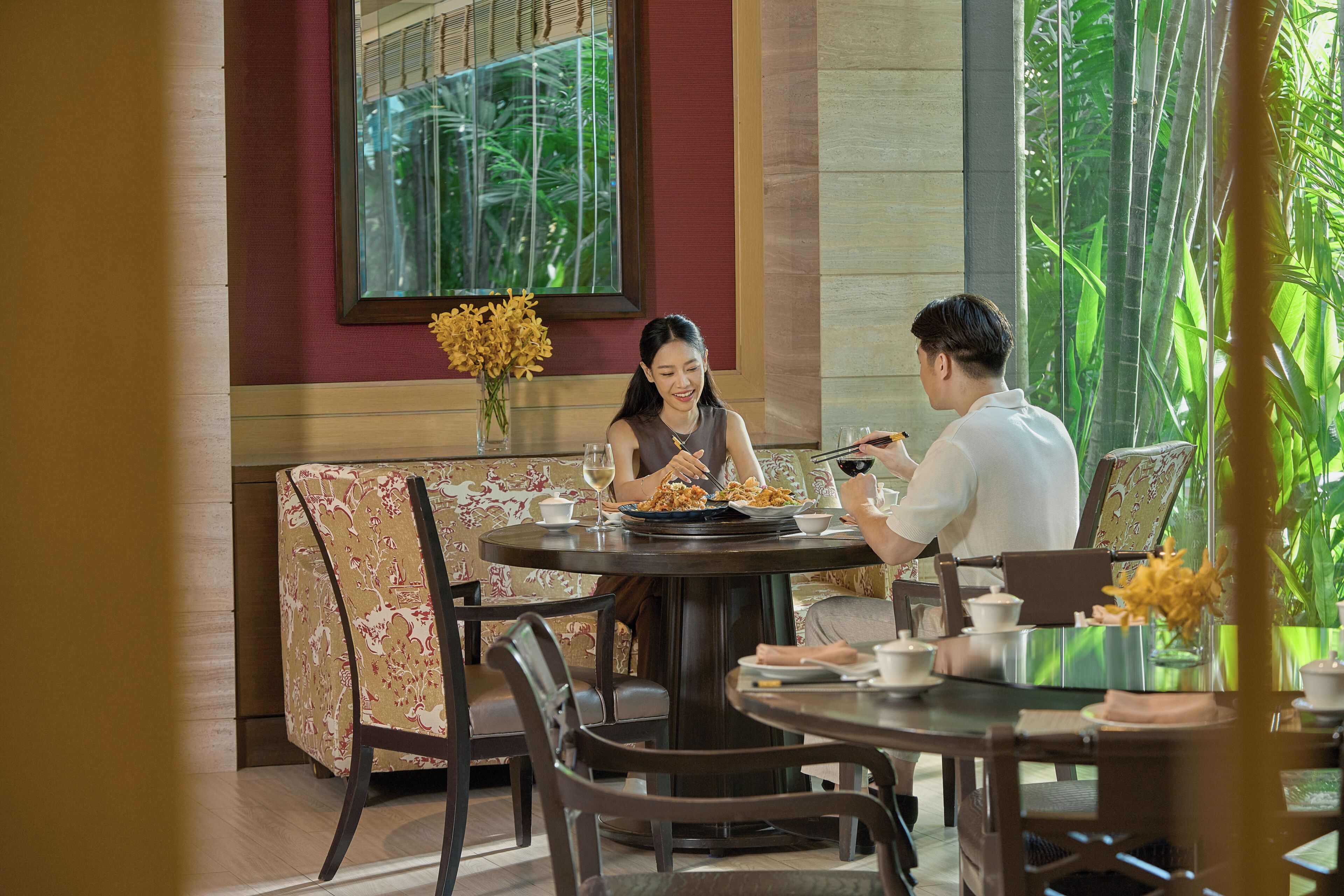 A dining area with a round table, chairs, a sofa, and a window with a view of greenery.