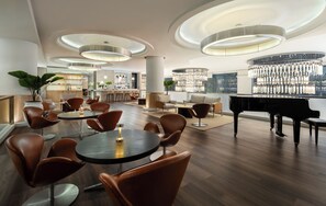 A modern lounge area with round tables, leather chairs, a grand piano, and a bar area. - Dusit Princess Srinakarin (Bangkok)