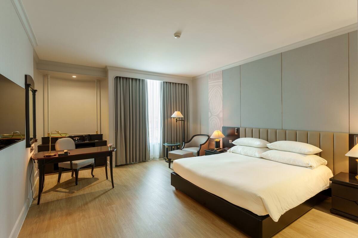 Ein Hotelzimmer mit Bett, Schreibtisch, Stuhl und einem kleinen Tisch mit Lampe.