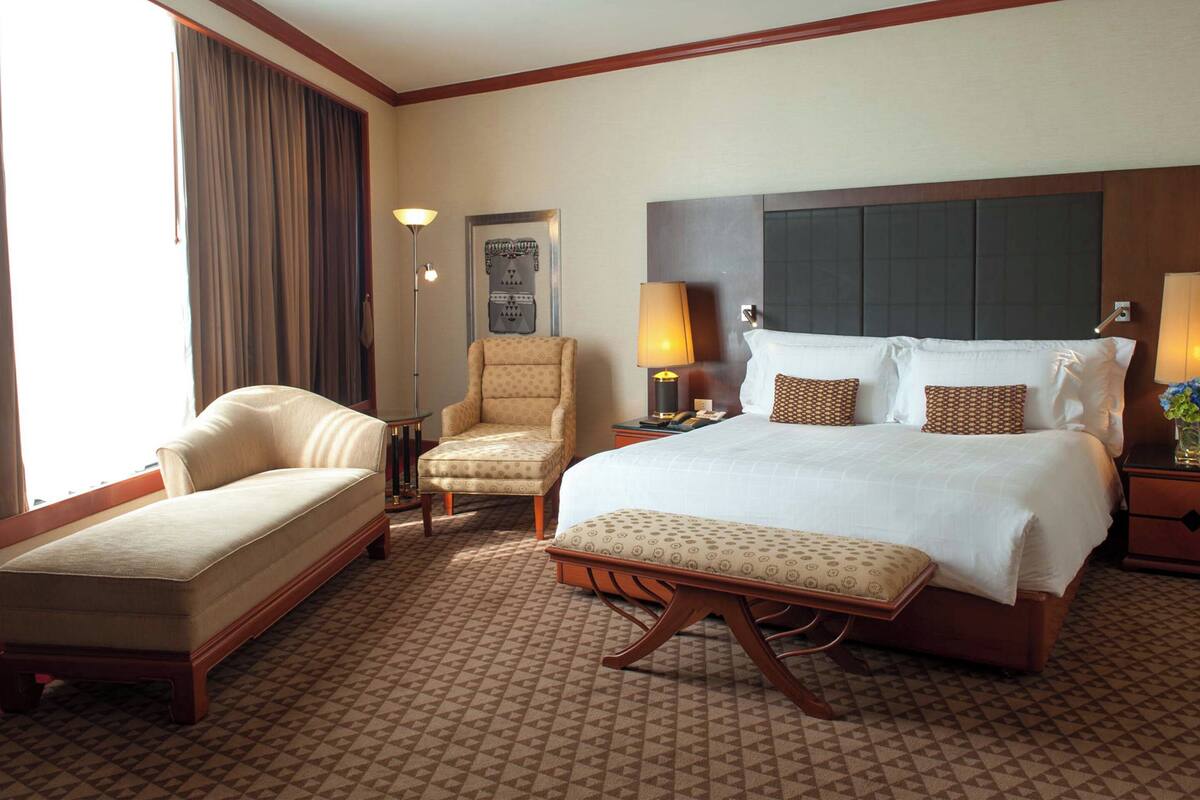 Ein Hotelzimmer mit einem großen Bett, zwei Sesseln, einem kleinen Tisch und einer Lampe.