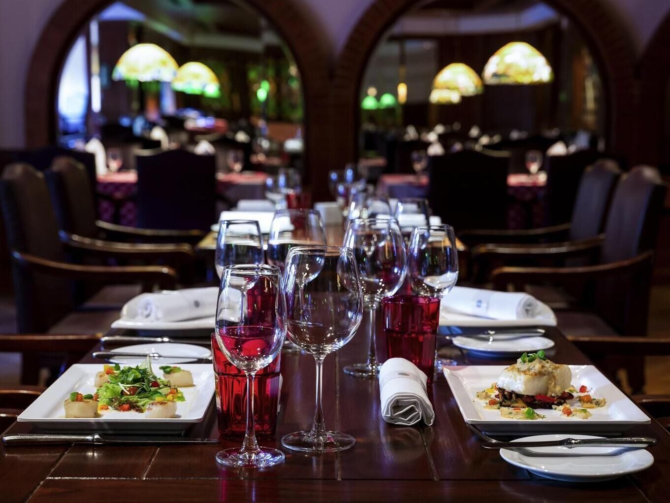 Une salle de restaurant avec des tables dressées pour le service, comprenant des verres à vin et des assiettes garnies de nourriture.