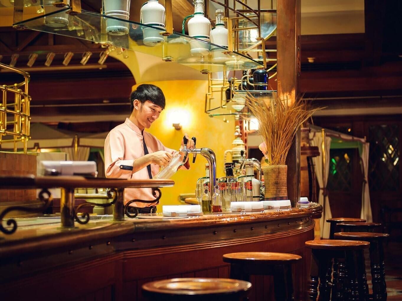 A bar area with a bartender preparing drinks, a counter with various bottles, and stools for seating.