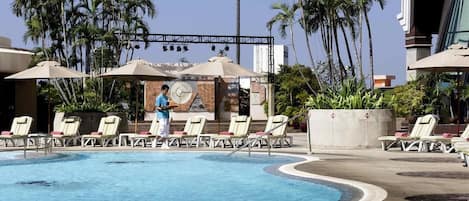 A pool area with lounge chairs and umbrellas, surrounded by palm trees.