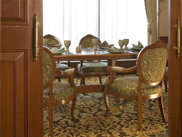 A dining area with a wooden table set for four, surrounded by upholstered chairs with patterned upholstery. - The Heritage Grand Khon Kaen Hotel (Khon Kaen)