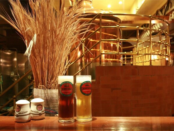 Two glasses of beer, a vase with wheat stalks, and two small cups on a wooden table in a bar setting. - The Heritage Grand Khon Kaen Hotel (Khon Kaen)