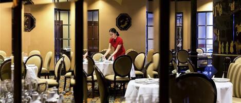 Un restaurante con mesas dispuestas para comer, un camarero atendiendo una mesa, y decoración tradicional.