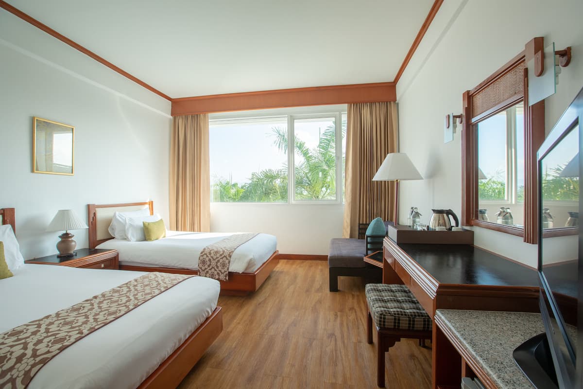 Une chambre d’hôtel avec deux lits, un bureau, une chaise, une télévision et une fenêtre avec des rideaux.