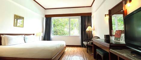Habitación de hotel con cama, escritorio, silla, televisor y ventana con cortinas.