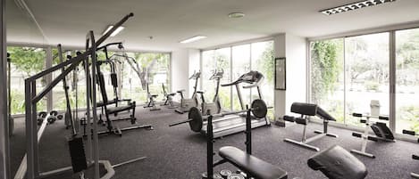 A gym with various exercise equipment, large windows, and a view of greenery outside.