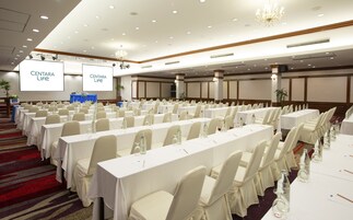 Un salón de conferencias con filas de mesas y sillas, una pantalla para proyector y una araña.