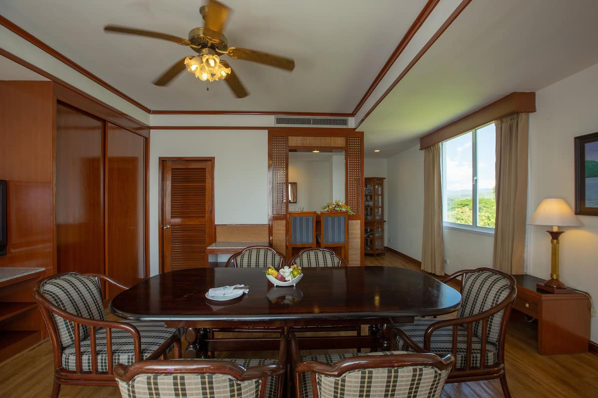 Un coin repas comprenant une table ronde, six chaises, un ventilateur de plafond et une fenêtre avec des rideaux.
