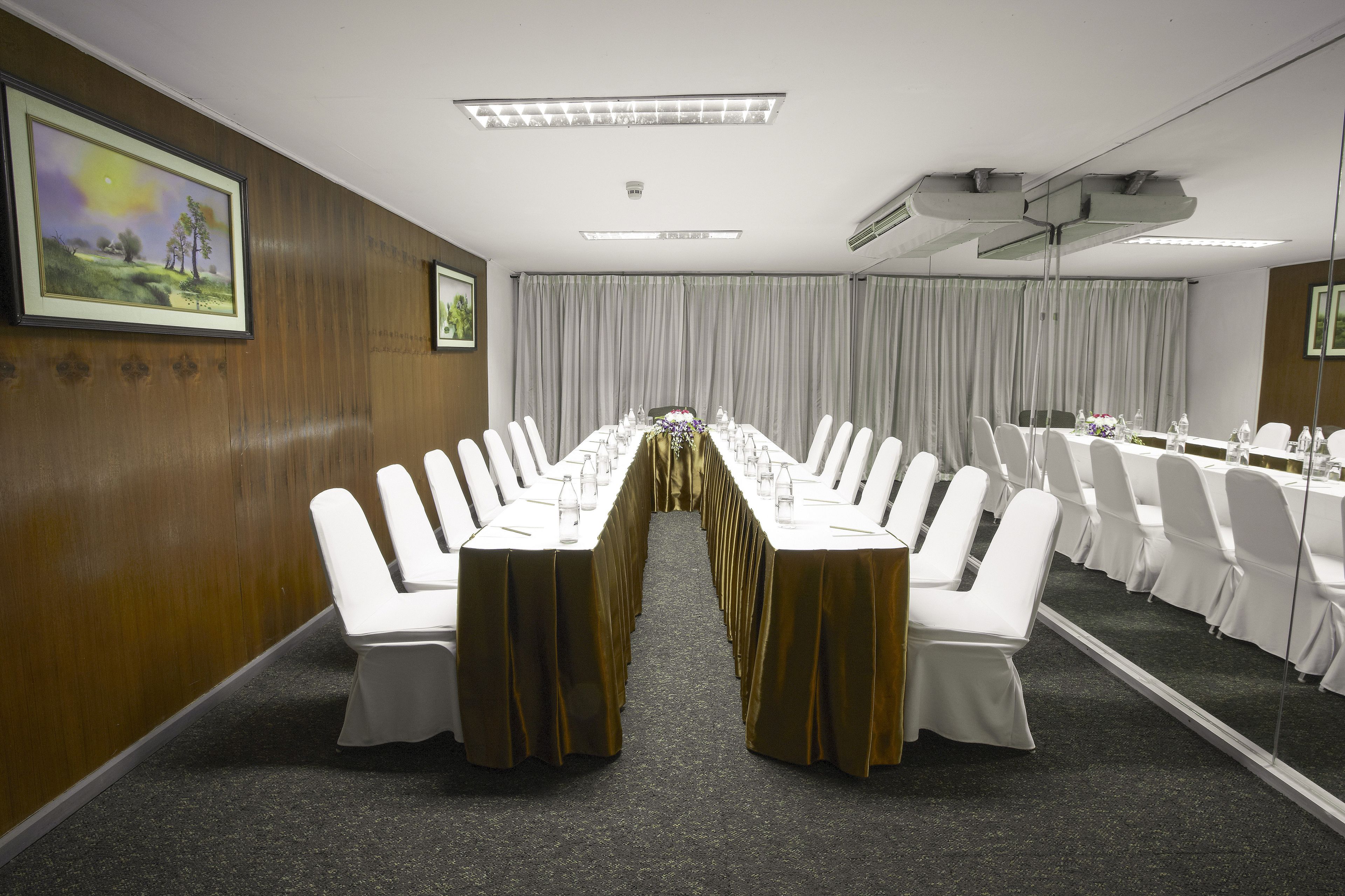Un salón de conferencias con largas mesas, sillas blancas y piso alfombrado.