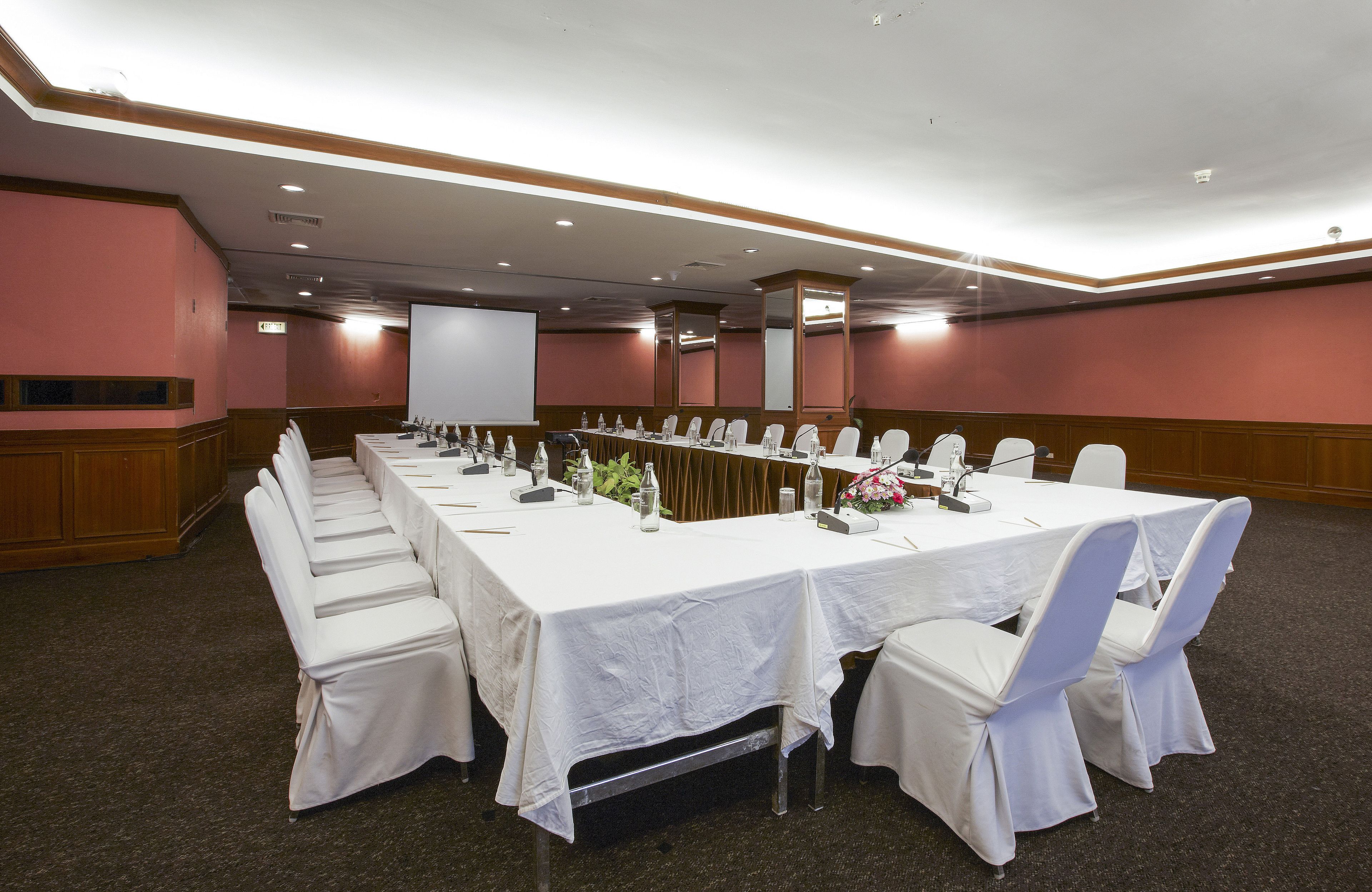 Ein Konferenzraum mit langem Tisch, weißen Stühlen und einer Projektionsleinwand.