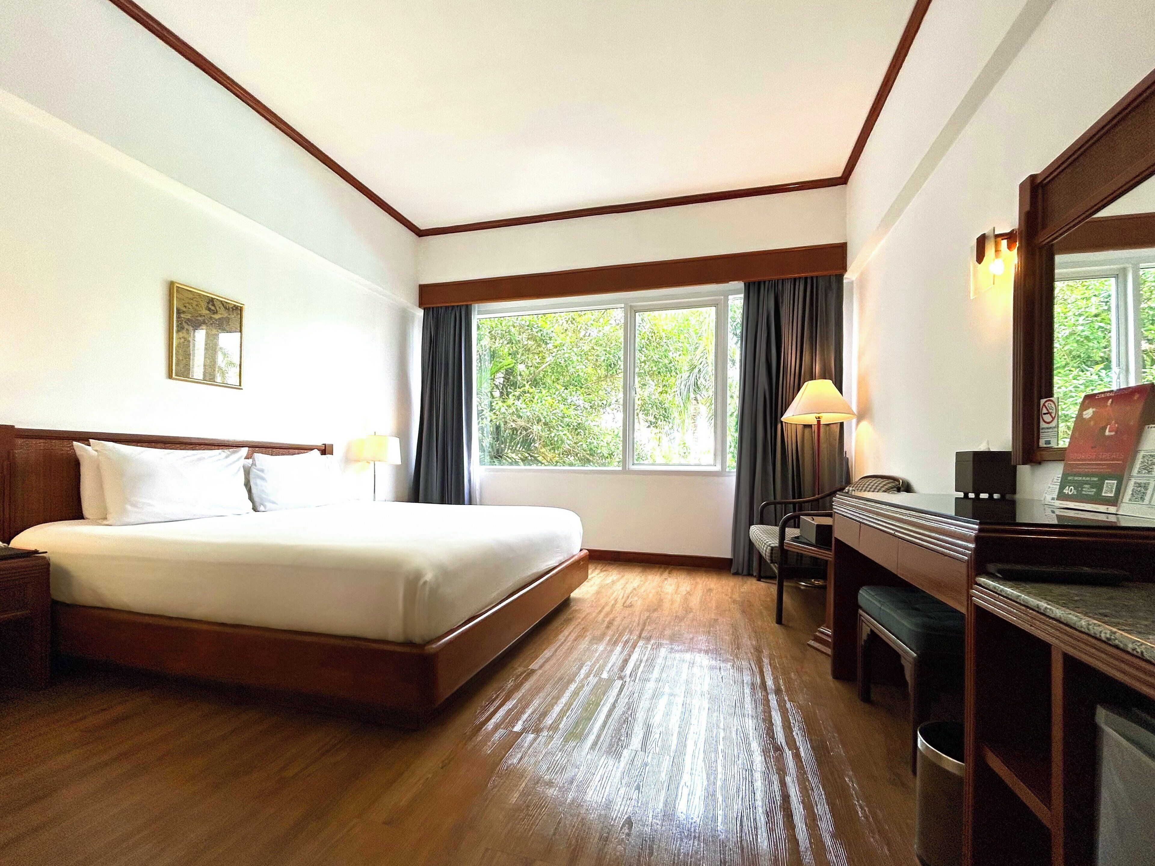 Una habitación de hotel con una cama grande, un escritorio, una silla, una lámpara y una ventana con cortinas.