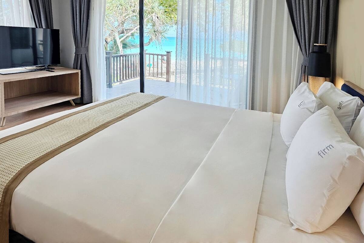Une chambre d’hôtel avec un grand lit, un téléviseur posé sur un meuble en bois et une vue sur la mer par de grandes fenêtres.