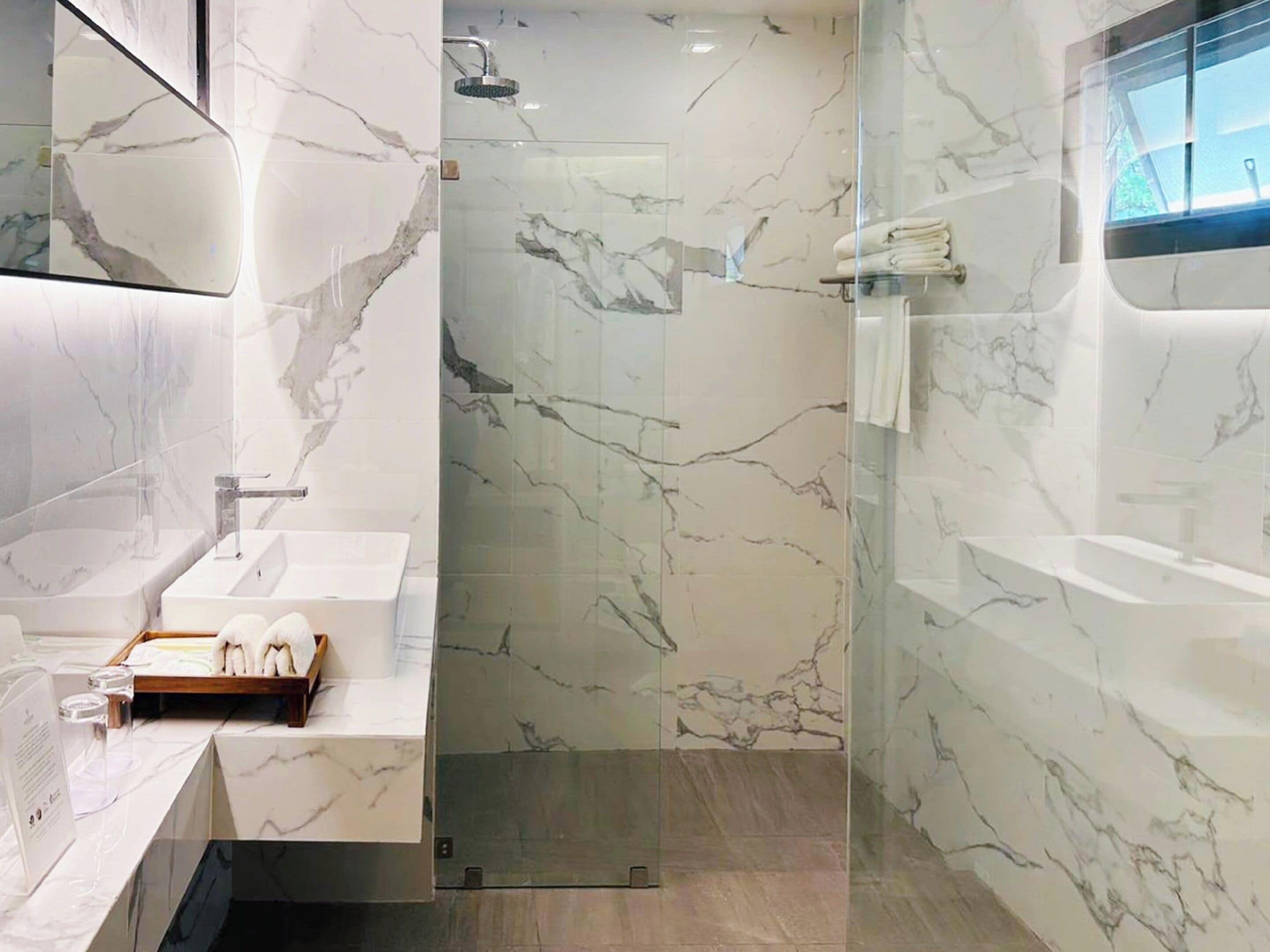 A modern bathroom with marble walls, a glass shower enclosure, and a vanity with toiletries.
