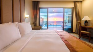 Habitación de hotel con una cama grande, un escritorio, una silla y vistas a la puesta de sol a través de las puertas del balcón.