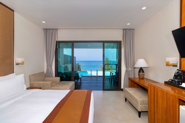 A hotel room with a bed, a sofa, a desk, a lamp, and a view of the ocean.