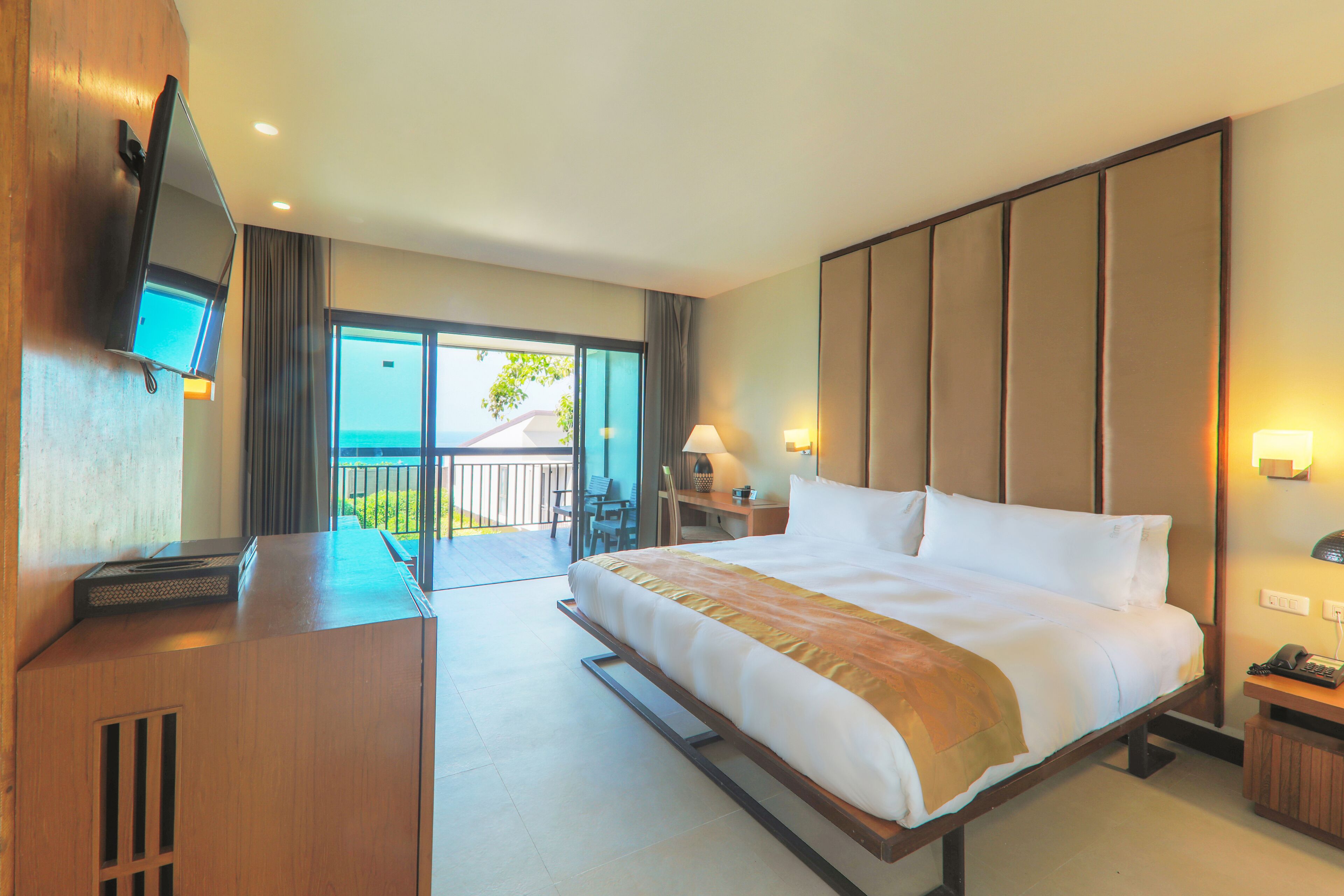 A hotel room with a large bed, a desk with a flat-screen TV, a desk lamp, and a view of the outdoors.