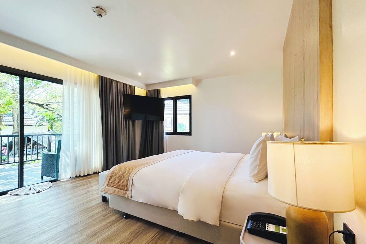 Une chambre d’hôtel moderne dotée d’un grand lit, d’un téléviseur à écran plat fixé au mur, d’une table de chevet avec une lampe et offrant une vue sur l’extérieur grâce à une porte-fenêtre coulissante.