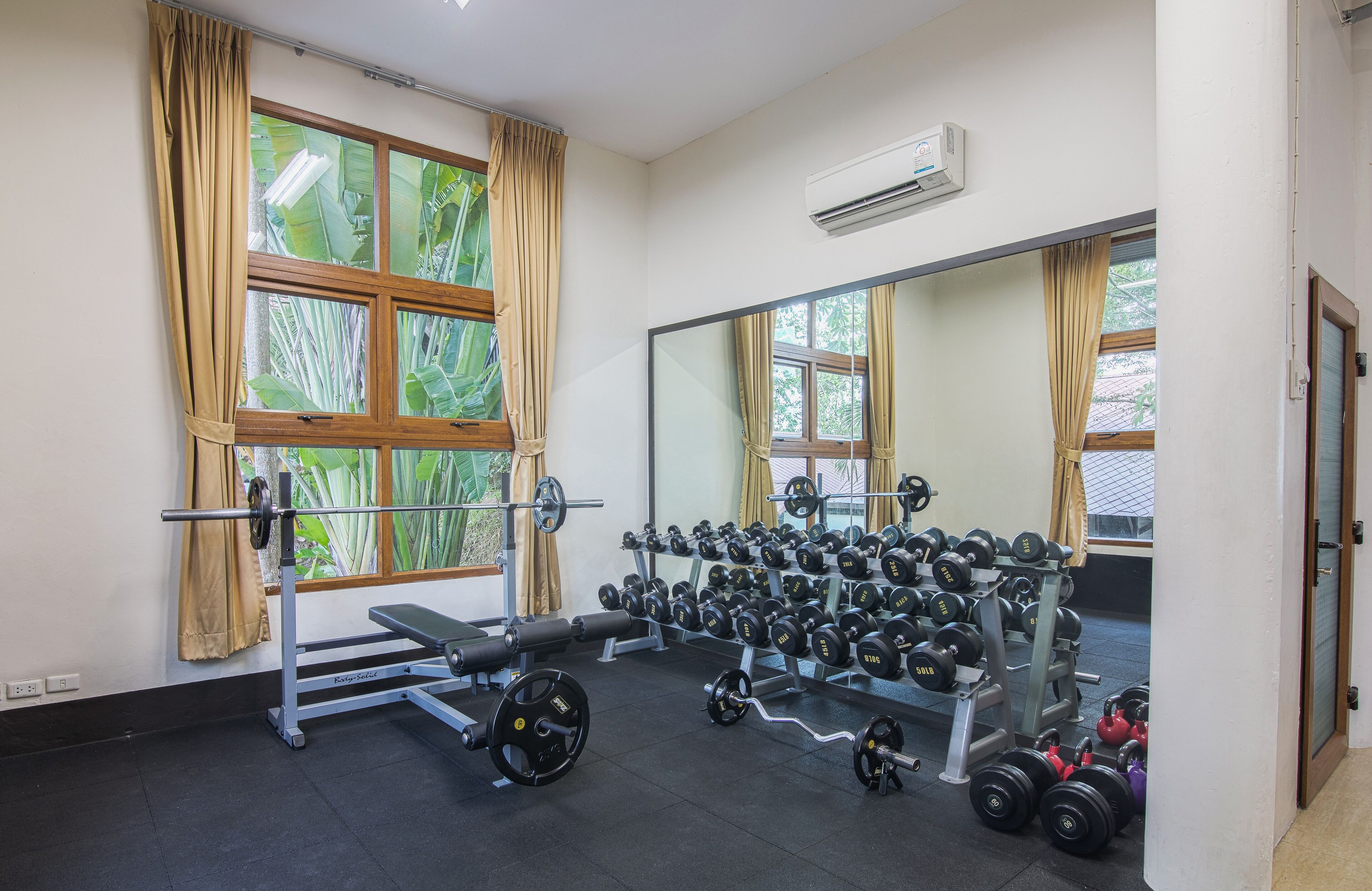 A gym with weightlifting equipment, a bench, and a mirror reflecting the room.