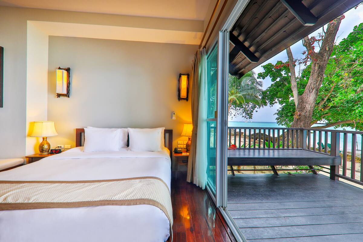 Une chambre d’hôtel avec un grand lit, des lampes de chevet, une vue sur l’océan et un balcon avec une balustrade.