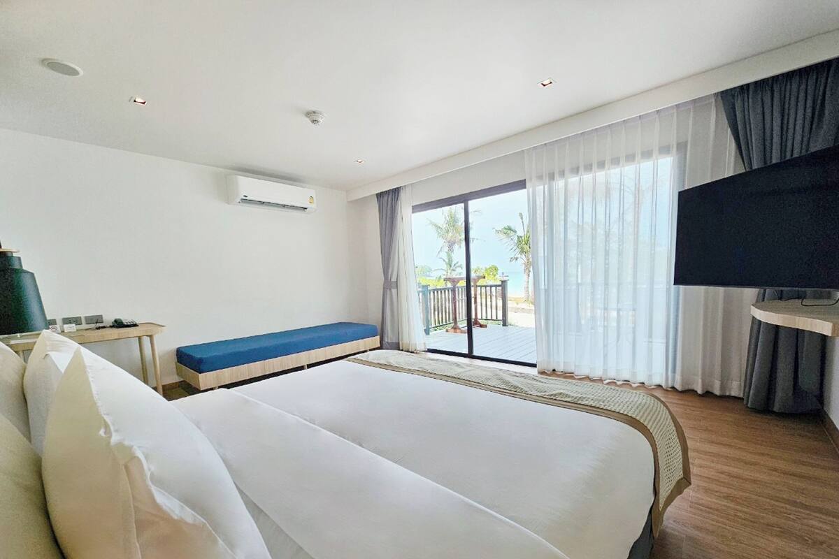 Une chambre d’hôtel avec un grand lit, un bureau, une télévision et un balcon donnant sur l’océan.