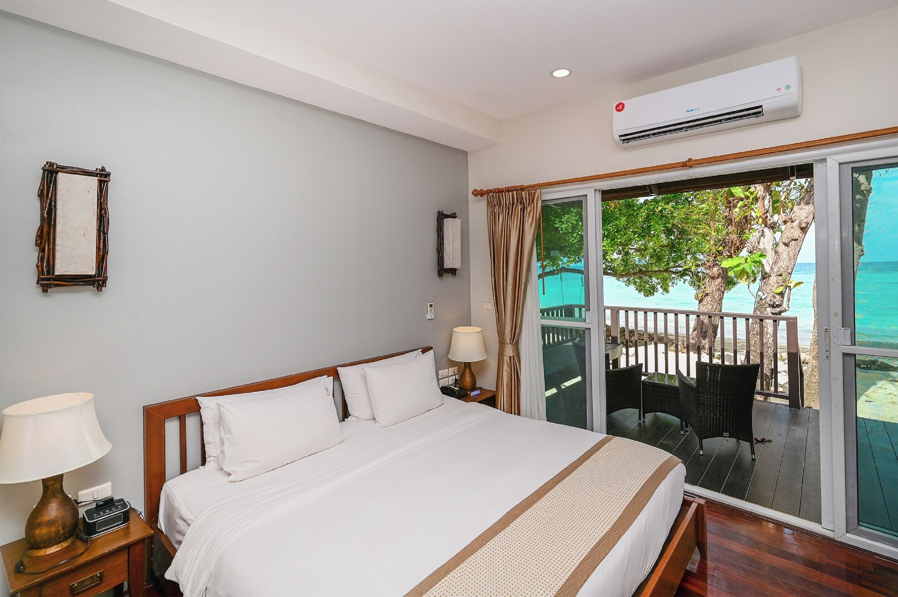 A hotel room with a bed, bedside lamps, a nightstand, a window with curtains, and a view of the beach.