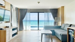 Una habitación de hotel moderna con un ventanal grande que ofrece vistas al mar, un sofá, una mesita, un televisor y un armario.