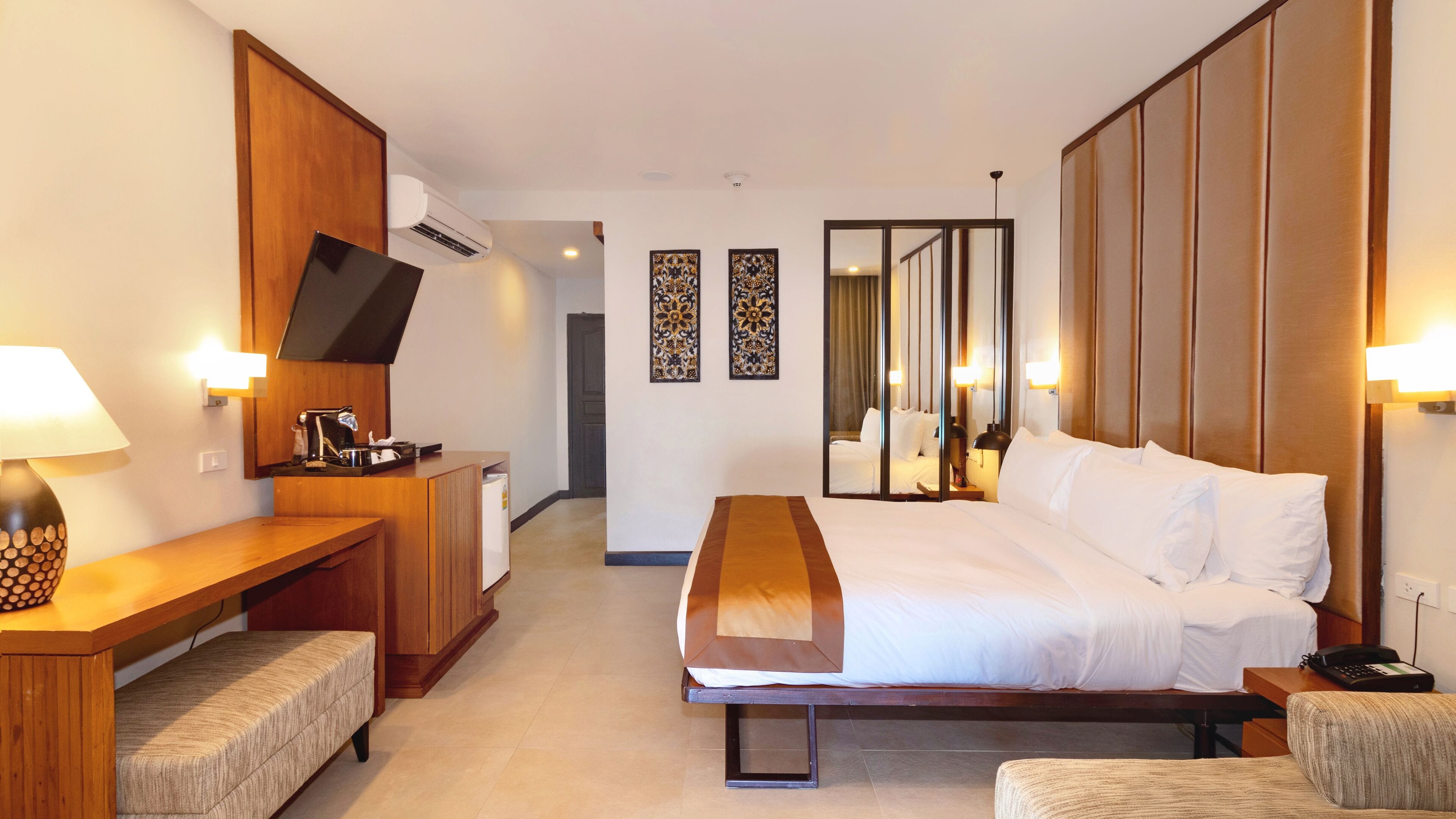 A hotel room with a bed, bedside table, lamp, desk, chair, and a small refrigerator.