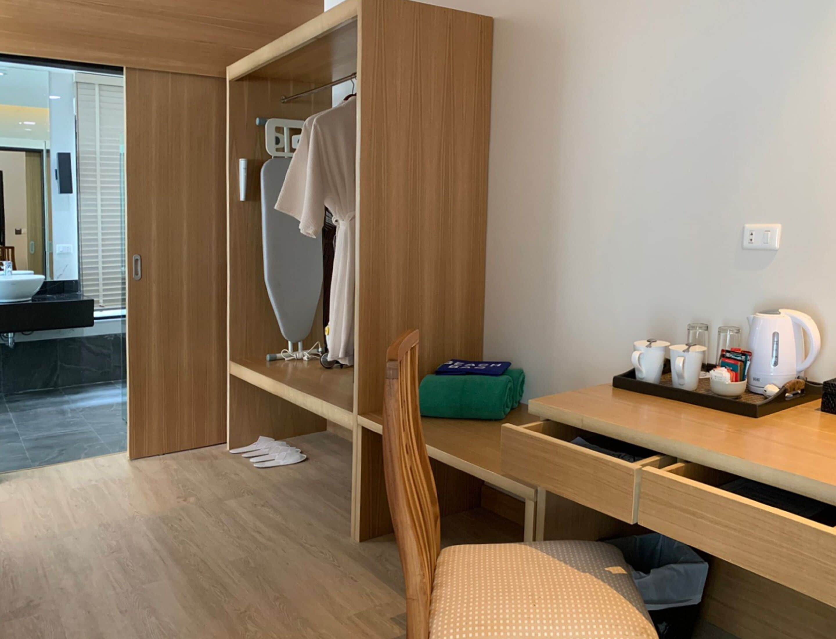 Habitación de hotel moderna con un armario de madera, un escritorio con una bandeja de desayuno, una silla y vistas al baño.